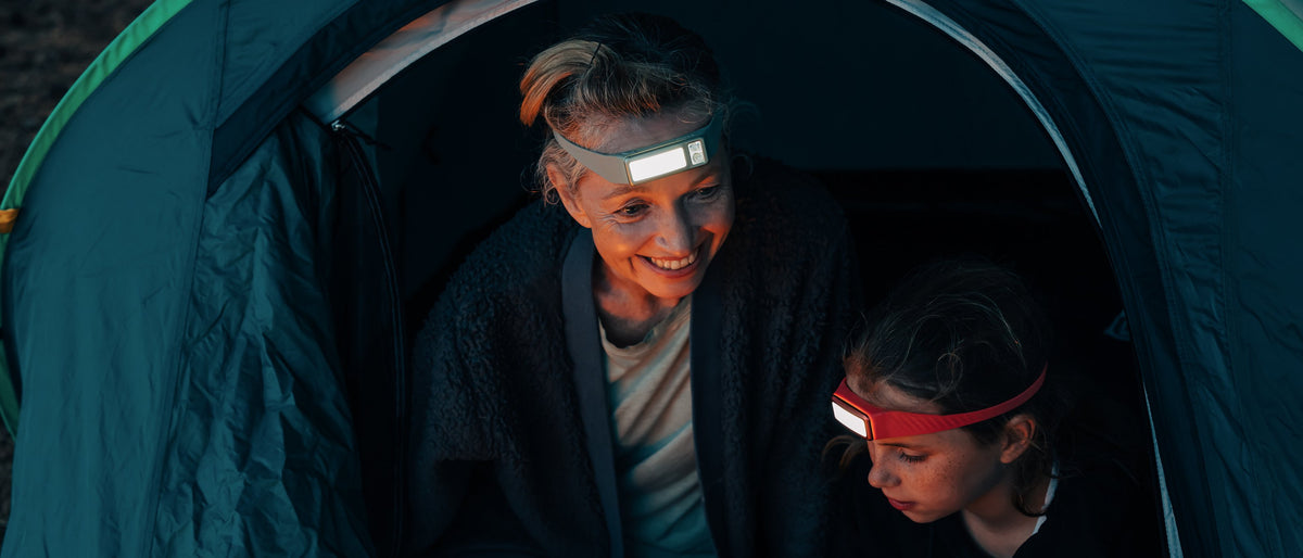 A girl and her mother at a tent at dusk, both wearing lit Scoutlite headlamps