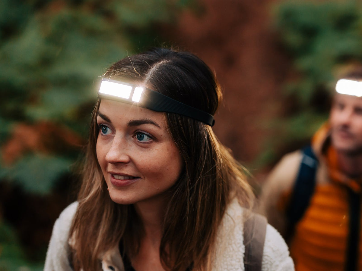 Two hikers in autumn woodland wearing lit Scoutlite headlamps