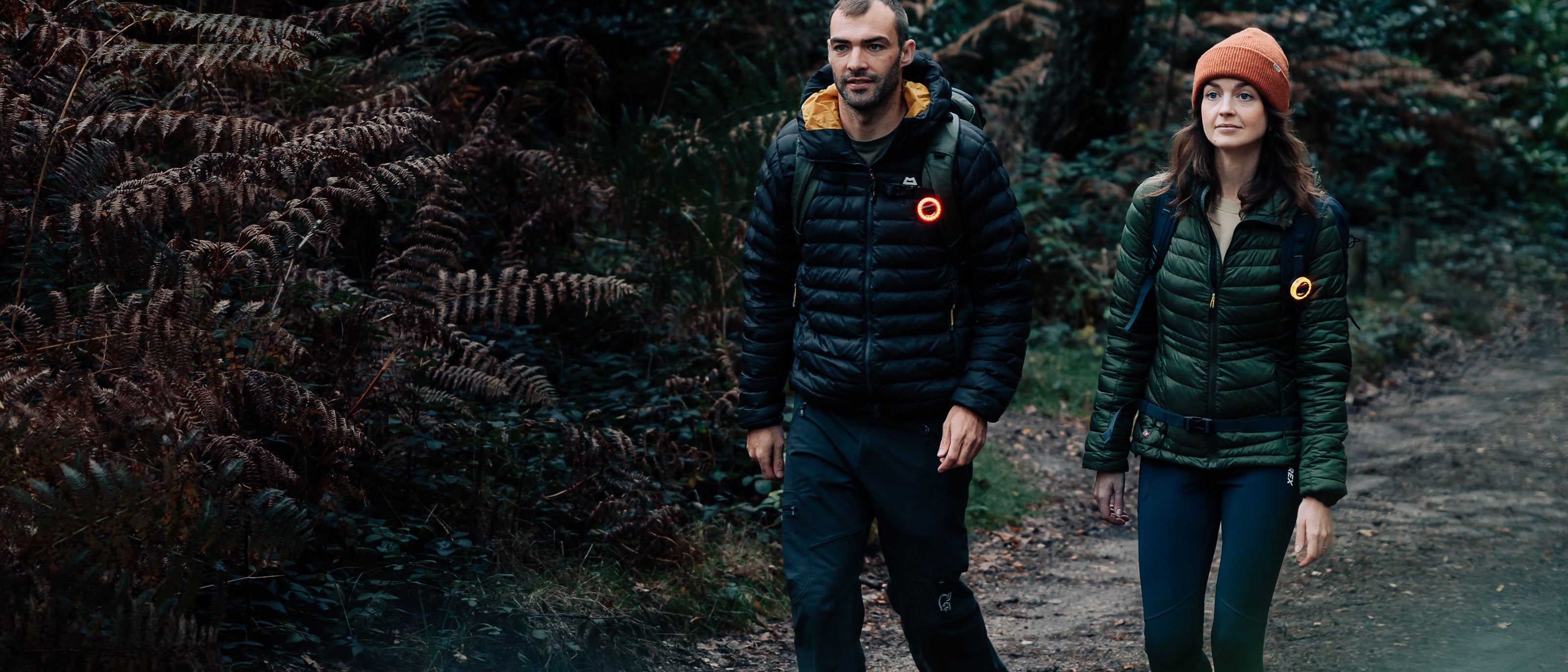 Two hikers at dusk wearing Scoutlite BlinkO wearable lights glowing on their jackets