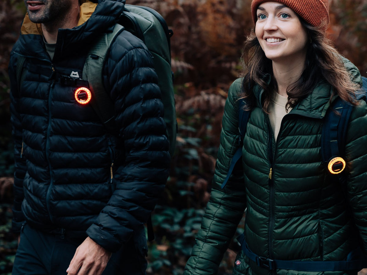 Two hikers at dusk wearing Scoutlite BlinkO wearable lights glowing on their jackets
